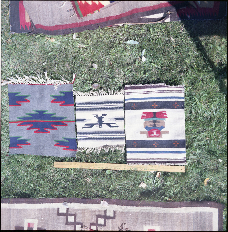 An image of many woven blankets or rugs created by unknown creators with a yard stick on one. Three are laid out next to a yard stick to show their size.