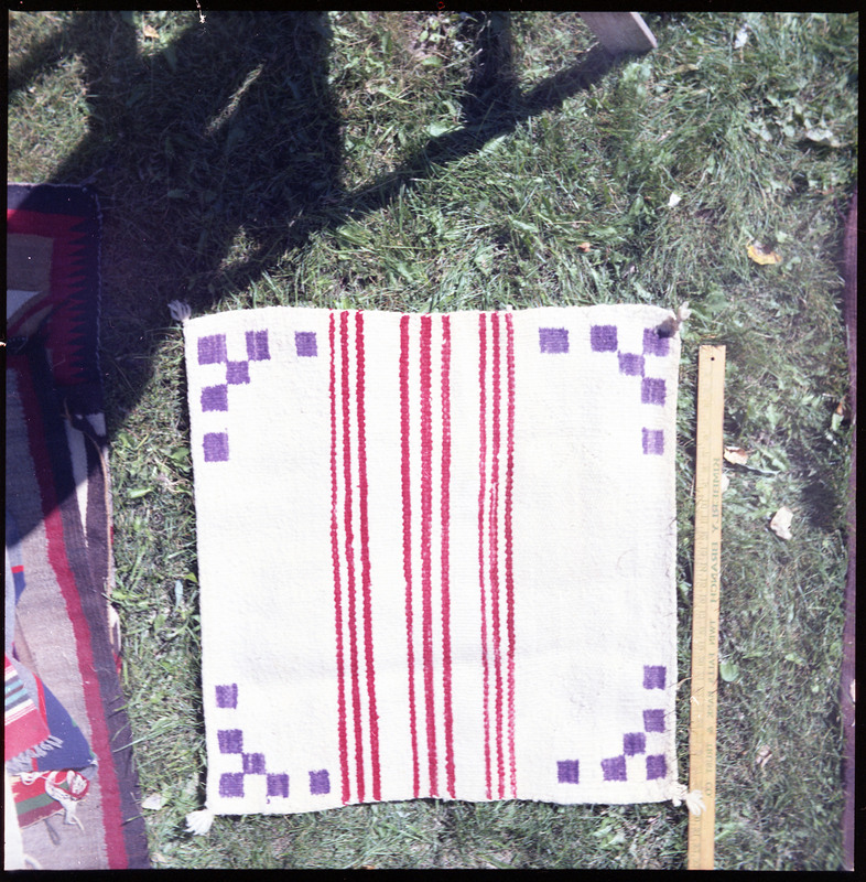An image of a woven blanket that is patterned, created by an unknown creator. The pattern is made up of blue, red, and white designs.