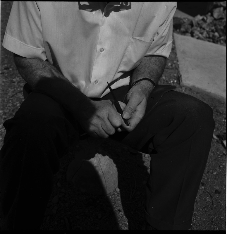 An image of Donald E. Crabtree flintknapping on a log stump. Crabtree is using a possibly bone tool to pressure flake the edge he just prepared by grounding it with the hammerstone.