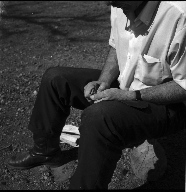 An image of Donald E. Crabtree flintknapping on a log stump. Crabtree is holding the stone object he is working with.