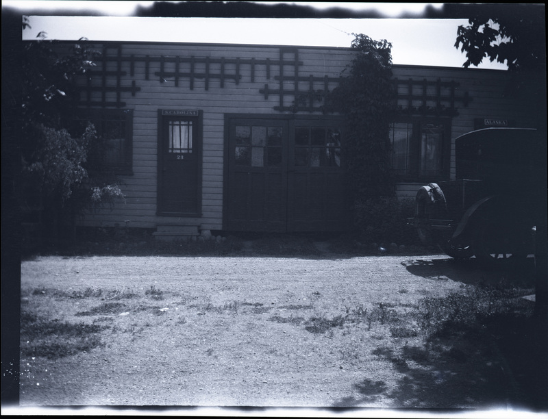 A black and white negative of a building with the label S Carolina 23 above the door. There is part of a car in the photo.
