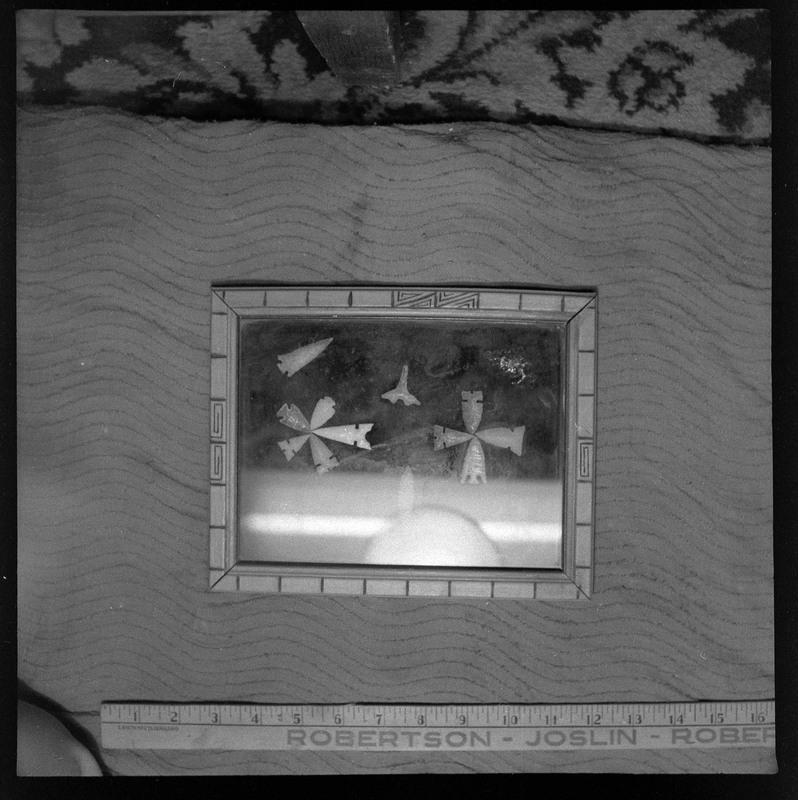 A black and white negative of a picture frame with bifaces in it arranged in circles. There are many variations of stone tools in this photo.
