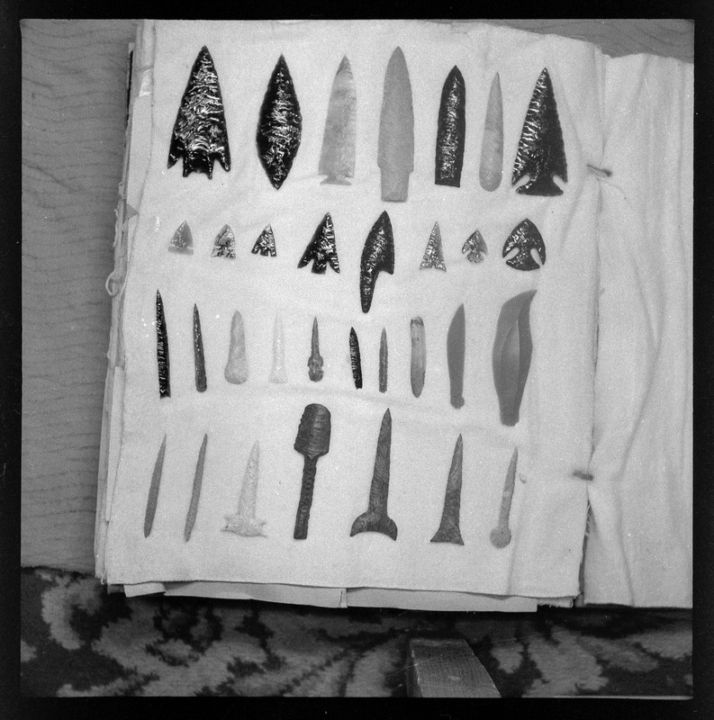 A black and white negative of stone tools laid out in rows. Many are bifaces, some blades but there is style variation. Many of these items remain in the collection, for example: Ce654 is the second item from right in the bottom row.