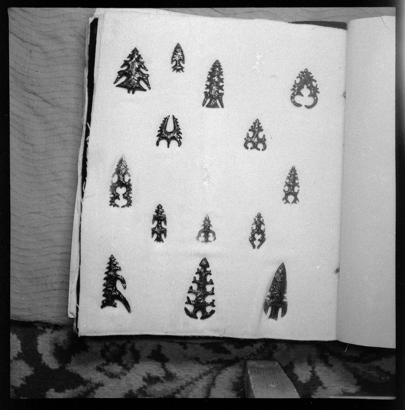 A black and white negative of eccentric stone tool items. There are different bifaces arranged neatly on white pages. They are all unique, detailed, and of different stone materials.