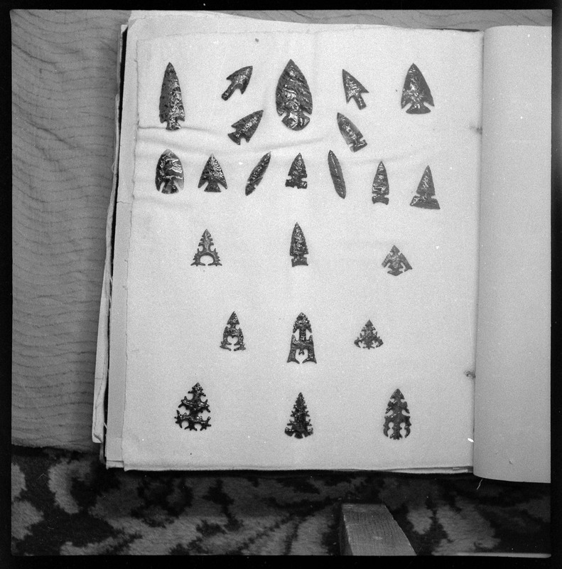 A black and white negative of eccentric stone tool items. There are different bifaces arranged neatly on white pages. They are all unique, detailed, and of different stone materials.