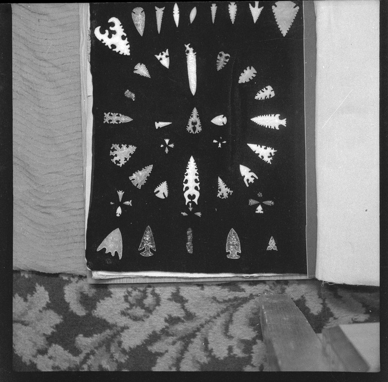 A black and white negative of eccentric stone tool items. There are different bifaces arranged neatly on black pages. They are all unique, detailed, and of different stone materials.