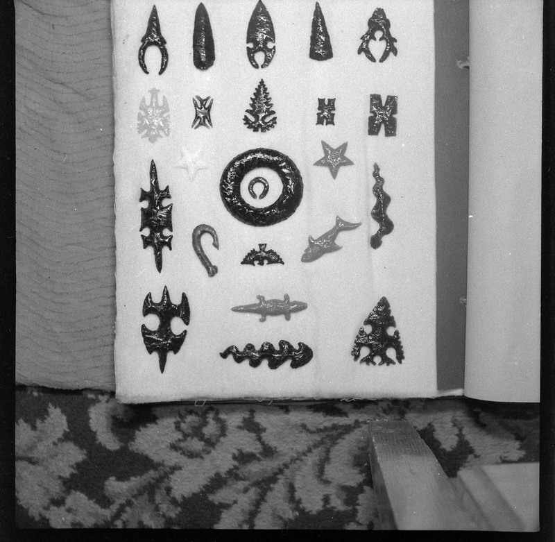 A black and white negative of eccentric stone tool items. There are different bifaces arranged neatly on black pages. They are all unique, detailed, and of different stone materials. The shark is Ce1480 and the snake at the bottom center is Ce 3500 and can both be seen as a 3D models.