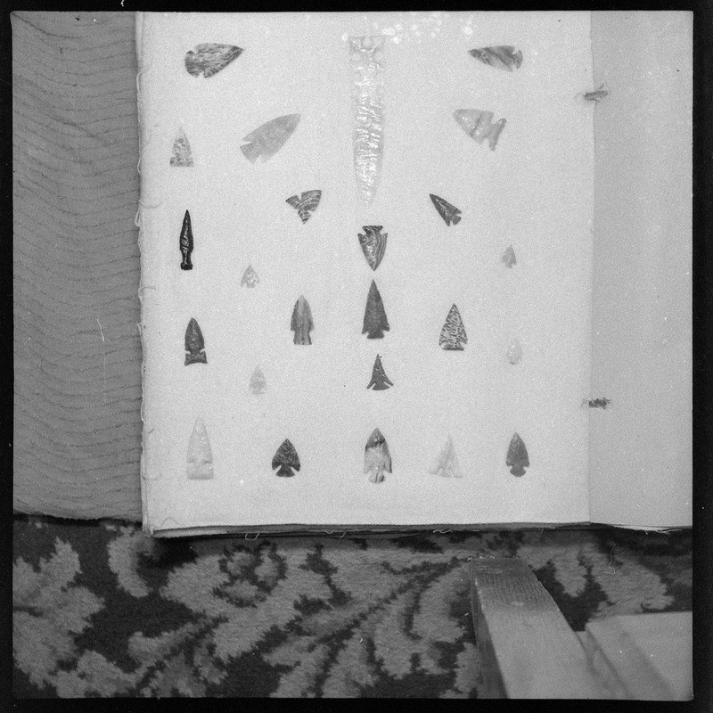 A black and white negative of eccentric stone tool items. There are different bifaces arranged neatly on white pages. They are all unique, detailed, and of different stone materials.