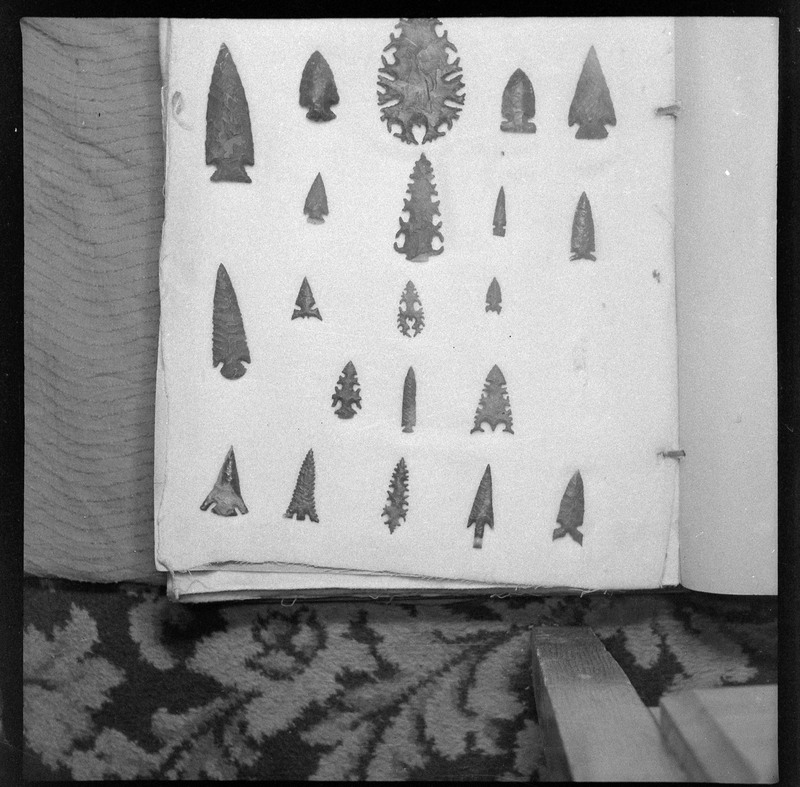 A black and white negative of eccentric stone tool items. There are different bifaces arranged neatly on white pages. They are all unique, detailed, and of different stone materials.