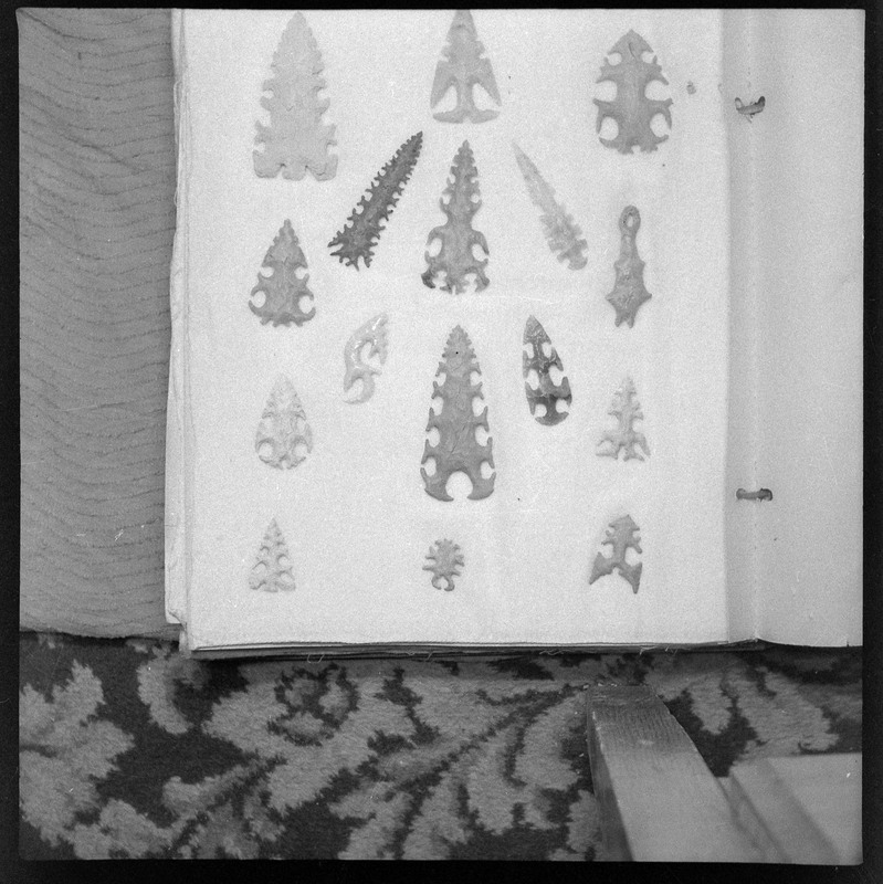 A black and white negative of eccentric stone tool items. There are different bifaces arranged neatly on white pages. They are all unique, detailed, and of different stone materials.