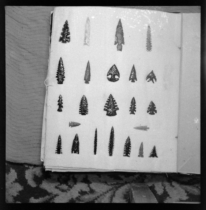 A black and white negative of eccentric stone tool items. There are different bifaces arranged neatly on white pages. They are all unique, detailed, and of different stone materials.