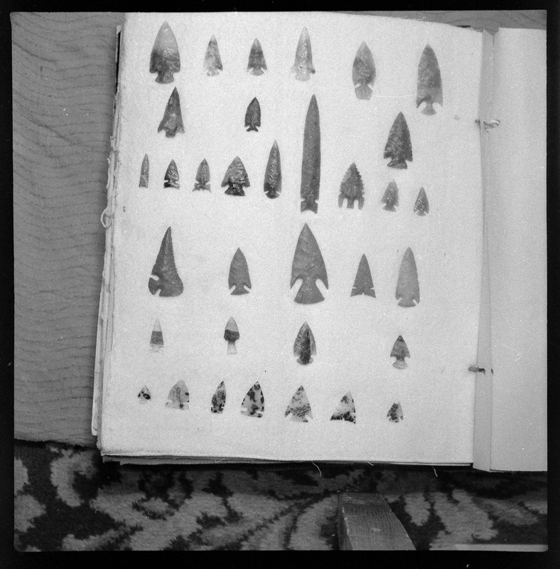 A black and white negative of eccentric stone tool items. There are different bifaces arranged neatly on white pages. They are all unique, detailed, and of different stone materials.