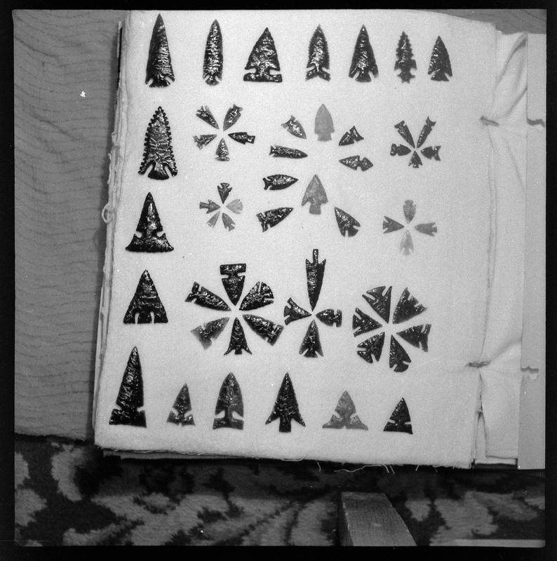 A black and white negative of eccentric stone tool items. There are different bifaces arranged neatly on white pages. They are all unique, detailed, and of different stone materials.