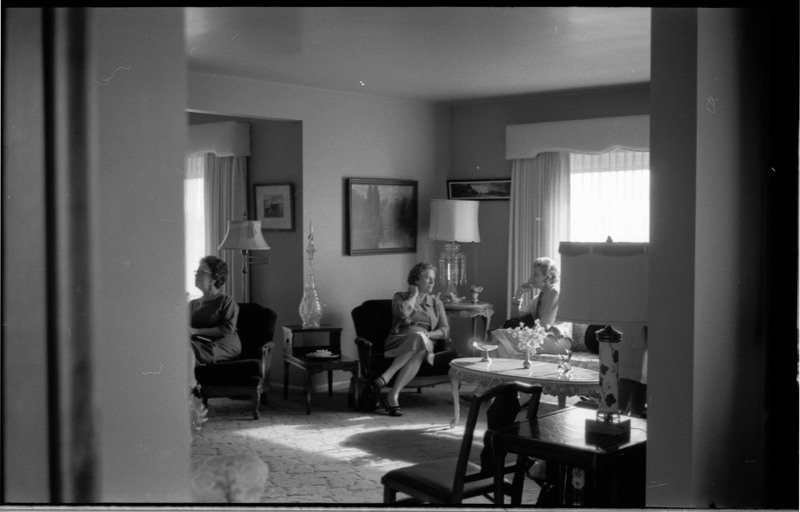 A photo of three women gathered in a sitting room. Two women are speaking with each other and one appear to be speaking with someone outside the camera's view. The event appears to be a bridal shower. Associated with item numbers: ce_b83_f1-item1-001 through ce_b83_f1-item1-016.