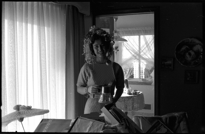 A photo of a woman posing for the camera and holding a gift. She has a hat of ribbons and bows in her hair. The event appears to be a bridal shower. Associated with item numbers: ce_b83_f1-item1-001 through ce_b83_f1-item1-016.