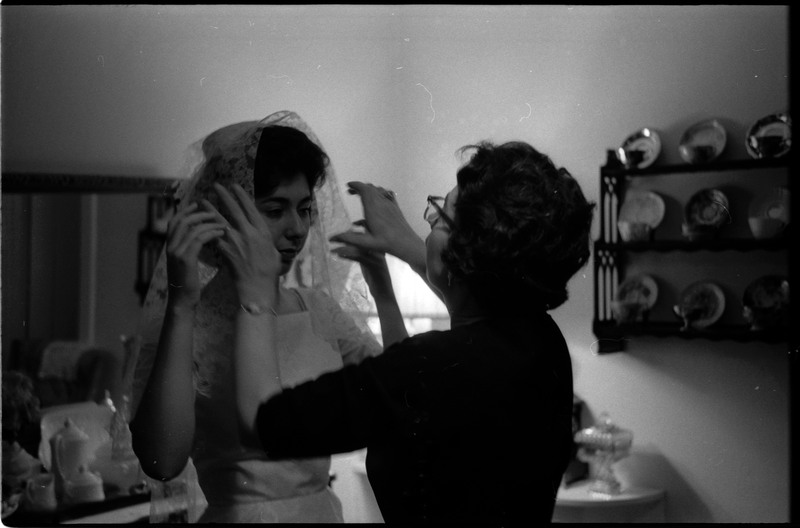A photo of a woman helping another woman in a wedding dress adjust her veil. Associated with item numbers: ce_b83_f1-item1-017 through ce_b83_f1-item1-036.