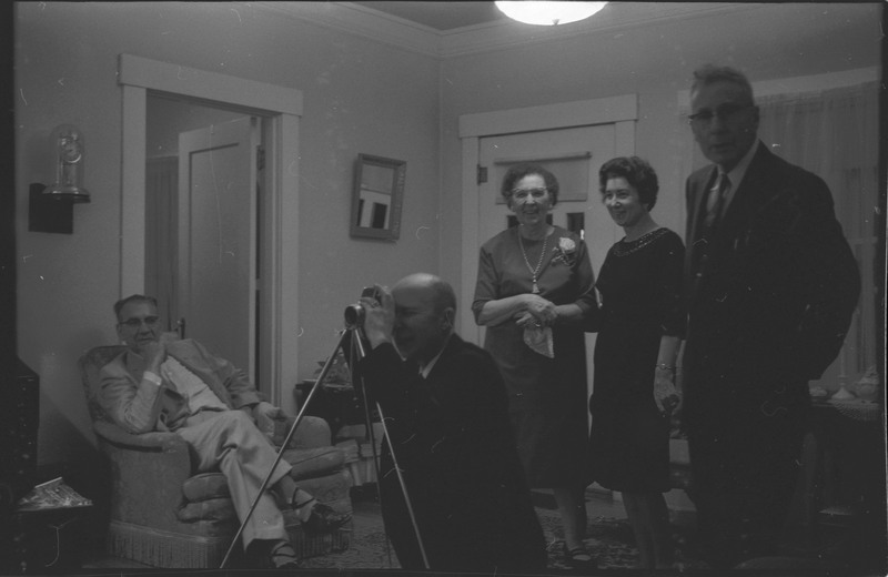 A photo of a group of five people in a sitting room, with one person taking a picture of someone outside the camera's view. Associated with item numbers: ce_b83_f1-item1-017 through ce_b83_f1-item1-036.