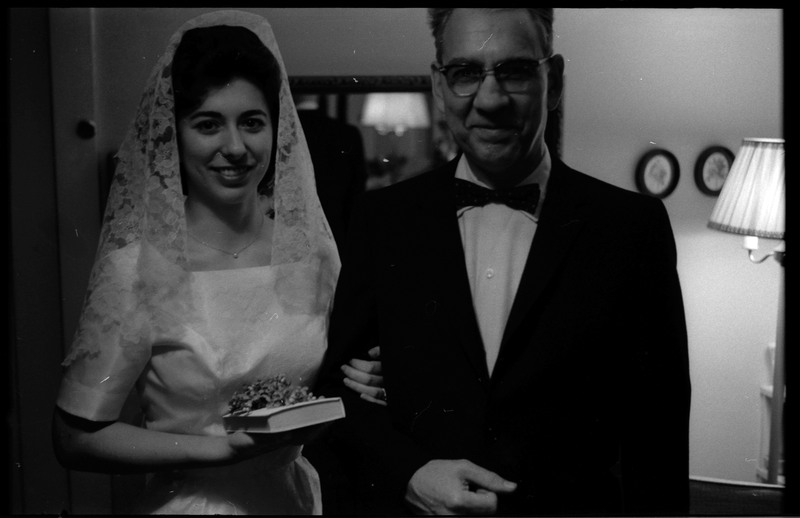 A photo of a woman wearing a wedding dress and a man wearing a suit smiling and posing for the camera. The woman is holding a book. Associated with item numbers: ce_b83_f1-item1-017 through ce_b83_f1-item1-036.