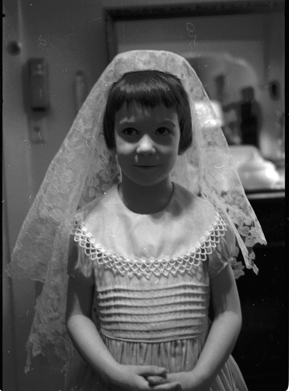 A photo of a child, wearing a dress and veil, posing for the camera. Associated with item numbers: ce_b83_f1-item1-017 through ce_b83_f1-item1-036.