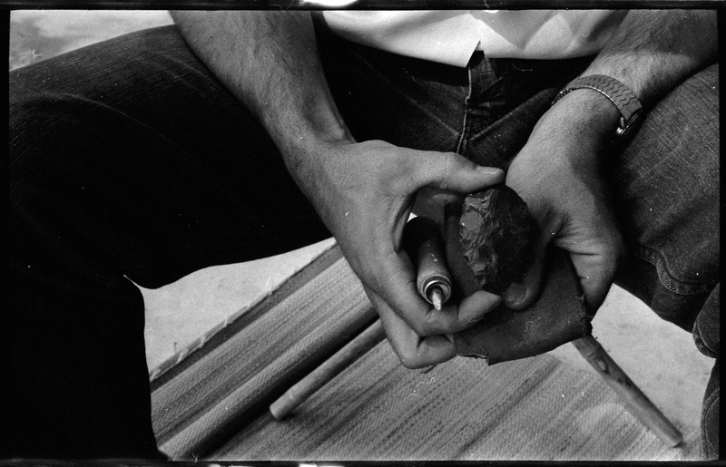 A photo of a pair of hands, holding a flintknapped piece and flintknapping tools. Associated with item numbers: ce_b83_f2-item1-004 through ce_b83_f2-item1-024.
