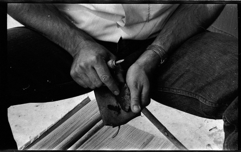 A photo of pair of hands, holding a stone and actively flintknapping. Associated with item numbers: ce_b83_f2-item1-004 through ce_b83_f2-item1-024.