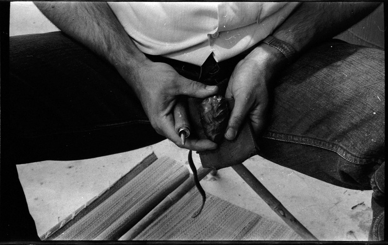A photo of pair of hands, holding a stone and actively flintknapping. Associated with item numbers: ce_b83_f2-item1-004 through ce_b83_f2-item1-024.