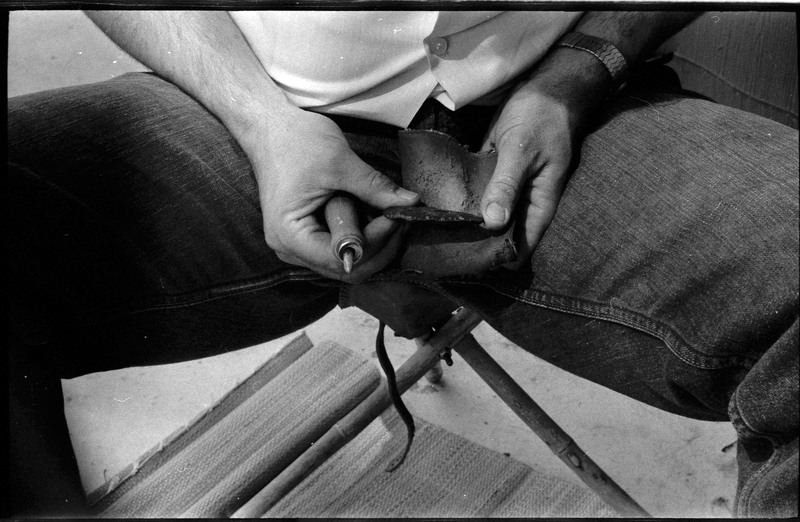 A photo of pair of hands, holding a stone and actively flintknapping. Associated with item numbers: ce_b83_f2-item1-004 through ce_b83_f2-item1-024.