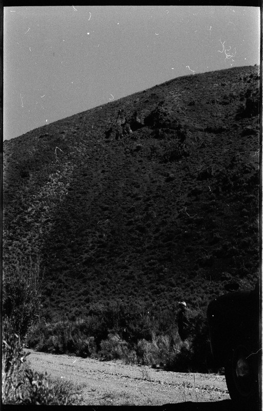 A photo of a hill behind a dirt or gravel road.