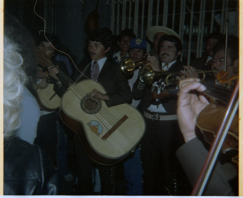 A photograph of a band playing music. The visible instruments include guitars, trumpets, and violins.