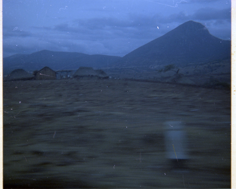 A photograph of a landscape with houses. A moutain is visible in the distance.