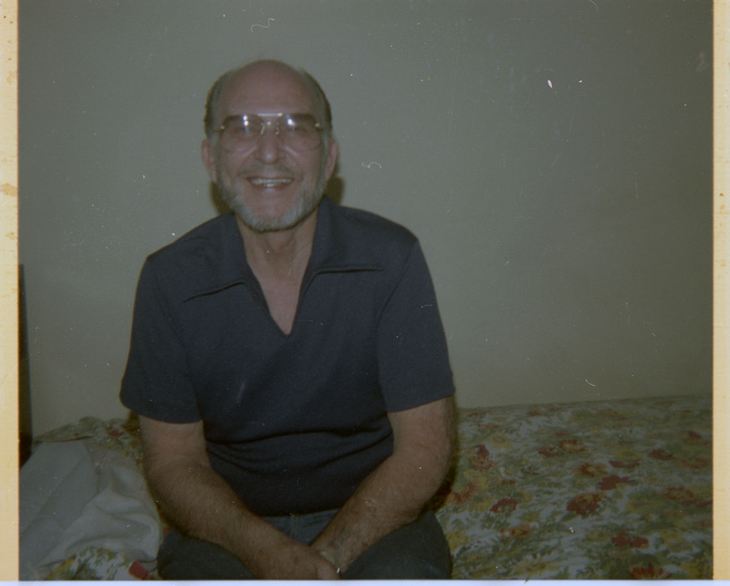 A photograph of Donald Crabtree sitting on a bed, smiling.
