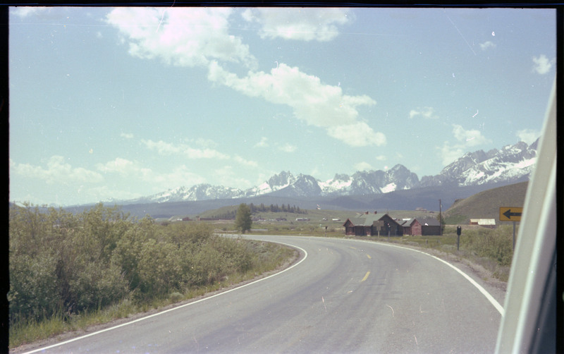 A photo taken from a vehicle of a landscape with a building and snowcapped mountains in the distance.