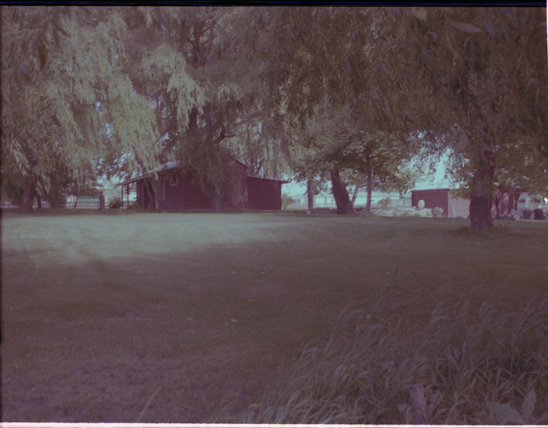 A photo of a home surrounded by a large grass yard and trees. Another building is visible on the right side of the image.