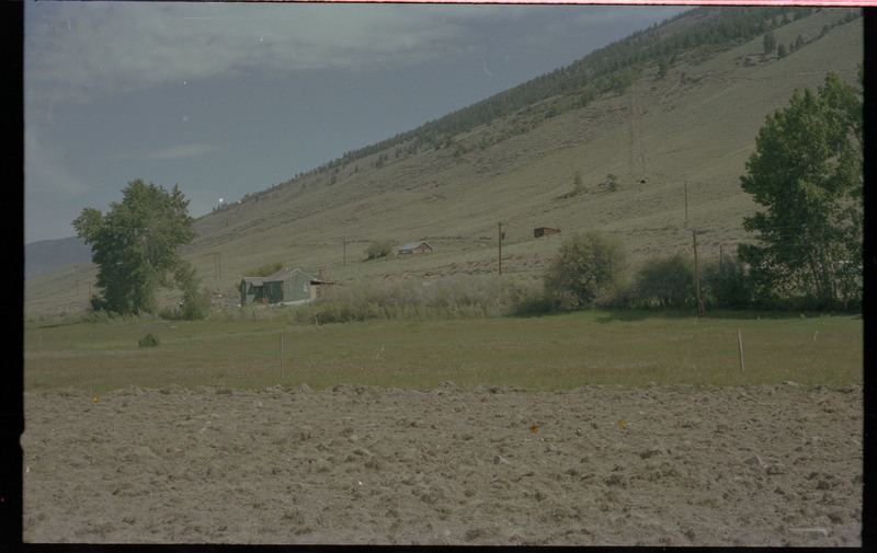 A photo of a hill with two homes and another structure.