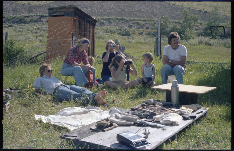 A photo of a group of people, including children, sitting outside around a ground-level table. The table appears to have different tools and materials. Associated item numbers: ce_b83_f2-item4-029 and ce_b83_f2-item4-031 through ce_b83_f2-item4-042.