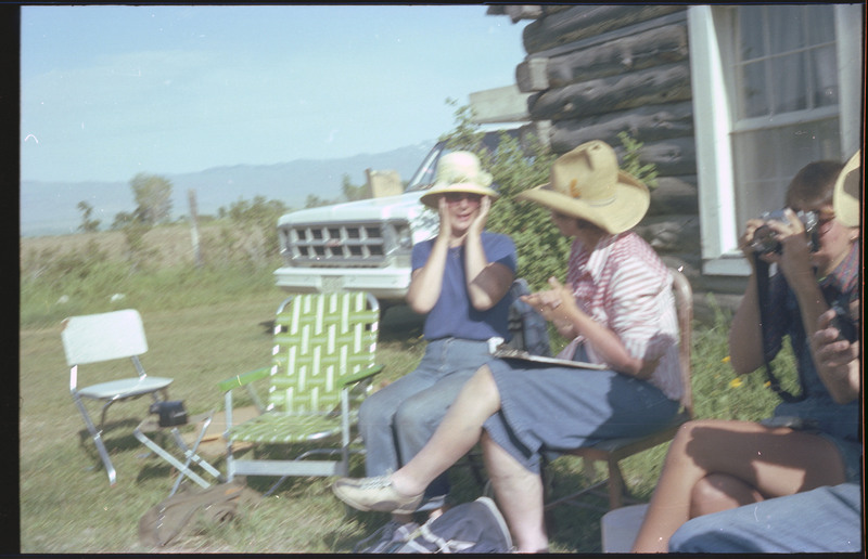 A photo of a group of people sitting outside, talking with one another. One person is taking photos. Associated item numbers: ce_b83_f2-item4-029 and ce_b83_f2-item4-031 through ce_b83_f2-item4-042.