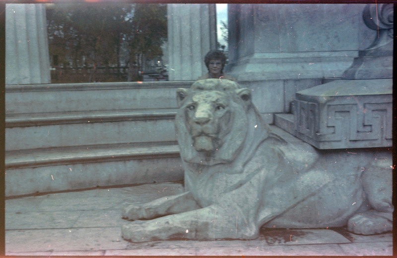 A photograph of a woman posing behind a statue of a lion.