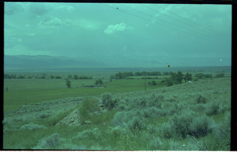 A photograph of a green landscape with mountains in the distance. A building, potentially a home, is also visible.