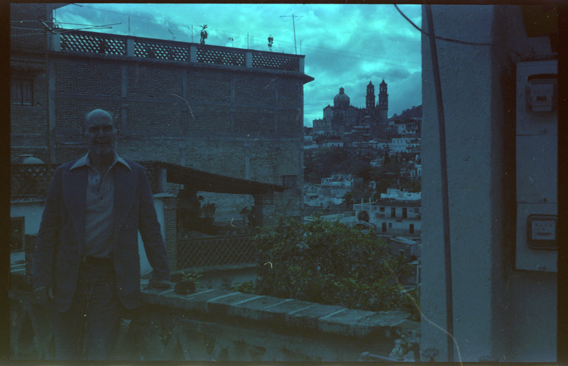 A photograph of Donald Crabtree standing near a stone wall, with city buildings in the distance.