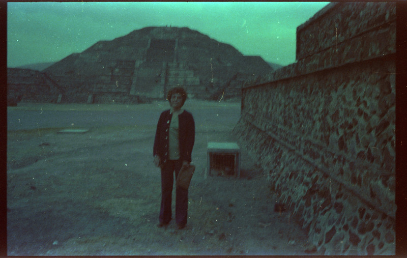 A photograph of Evelyn Crabtree standing next to a stone wall with the Pyramid of the Sun in the distance.