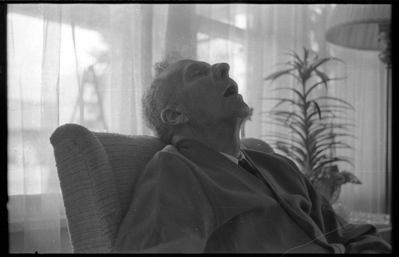 A closeup photograph of a man, who appears to be sleeping, in a sitting or living room.