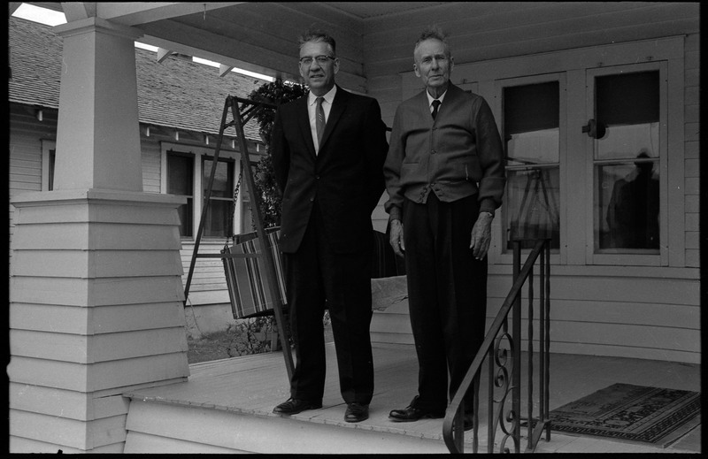 A photograph of two men standing on a porch. A porch swing is visble behind them.