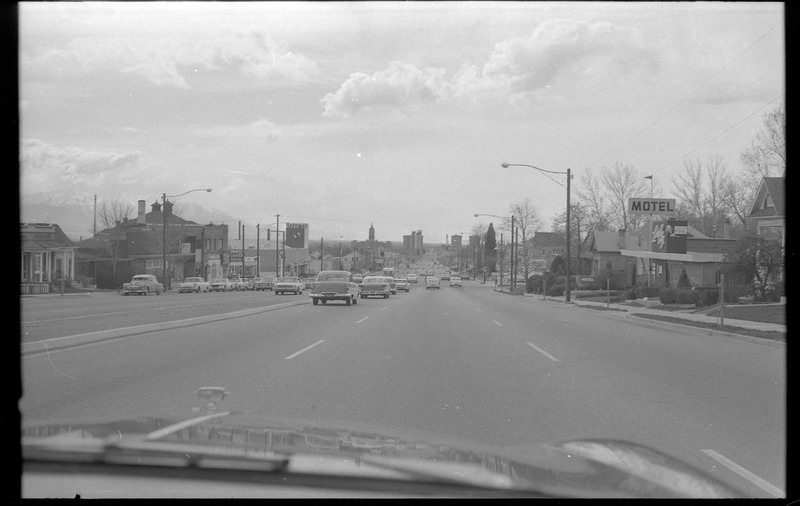 A photograph of cars driving on the road, with various building visible on each side of the image.