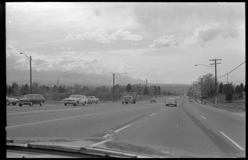 A photograph of cars driving on the road, with snowcapped mountain visible in the distance.