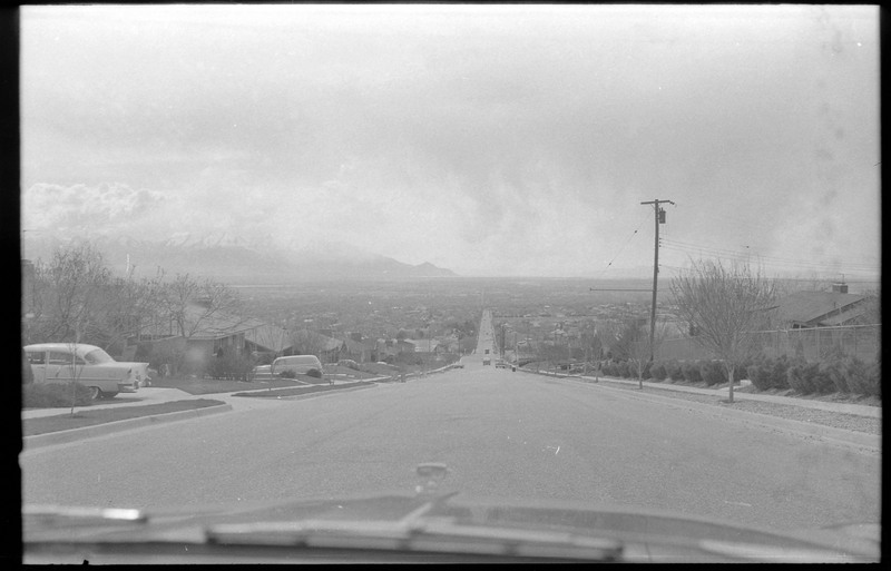 A photograph of homes lining a street, with snow-capped mountains in the distance. It appears that this photograph was taken from inside a vehicle.