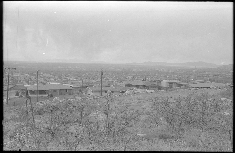 A photograph of undeveloped land with houses and other buildings in the distance.