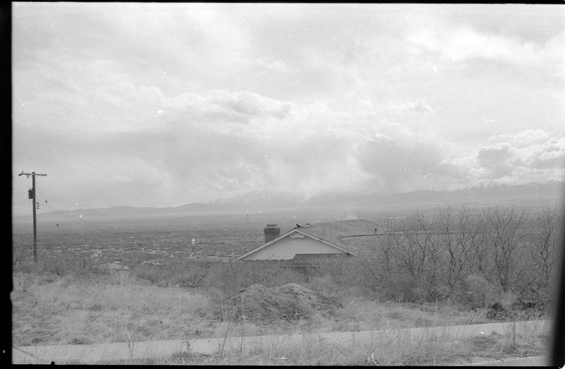 A photograph of undeveloped land with a house and other buildings in the distance.