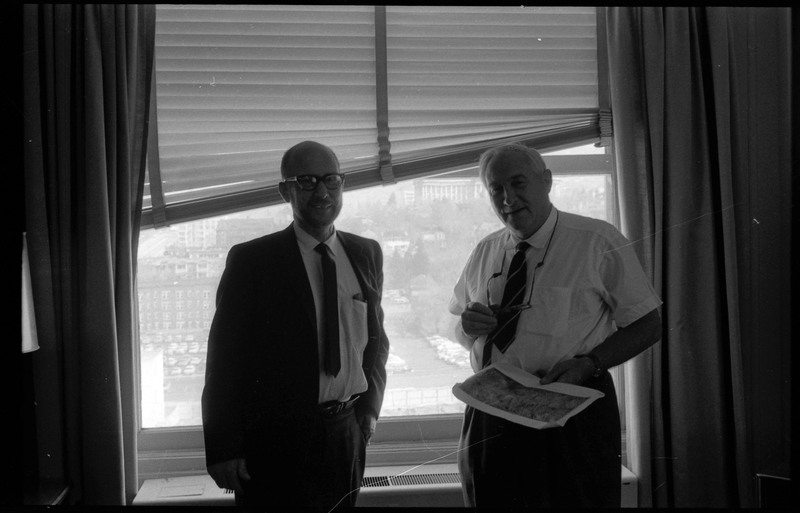 A photograph of Donald Crabtree and an unnamed man standing and posing for the camera. The unnamed man is holding what appears to be a document in his hand.