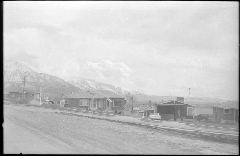 A photograph of homes lining a street, with snow-capped mountains in the distance.