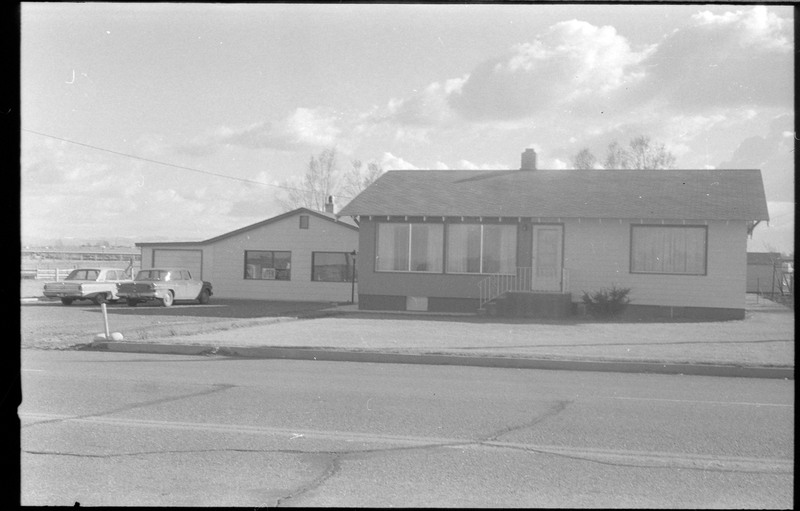 A photograph of a home and outbuilding. The outbuilding has two cars parked in front and an "Open" sign is visible in the window.